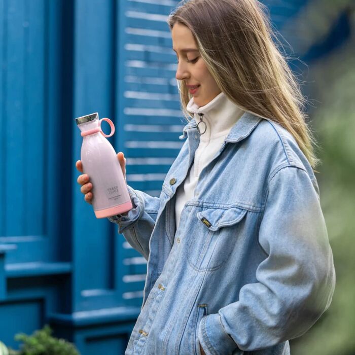 Une femme souriante tenant un Mixeur Fresh Juice rose et regardant un smoothie mauve fraîchement préparé. Le robot de cuisine est sans fil