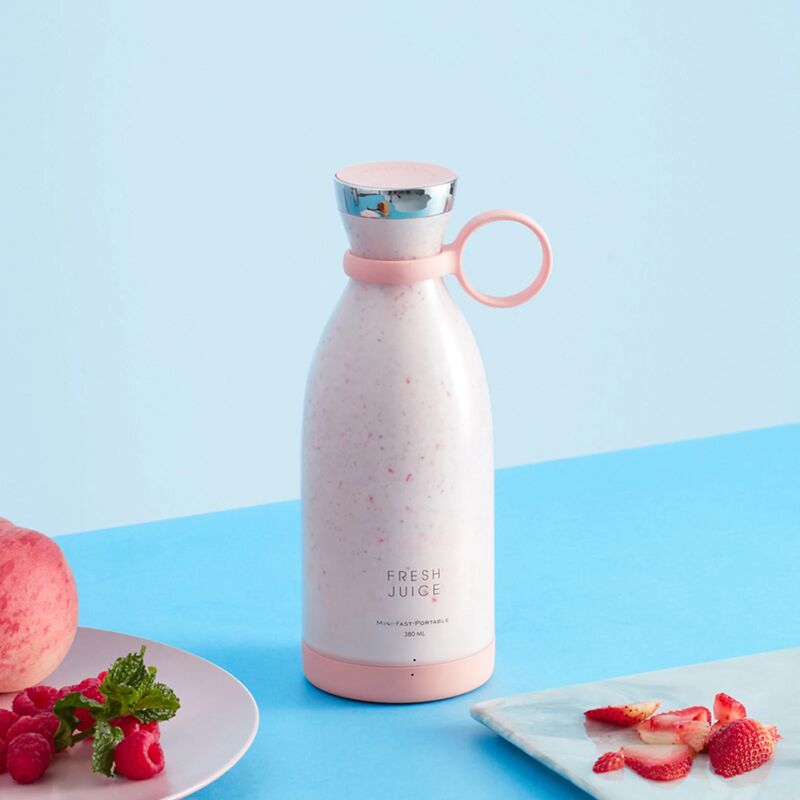 A pink Fresh Juice portable blender filled with a pink and white smoothie, surrounded by dishes containing raspberries, strawberries and peaches on a blue background.