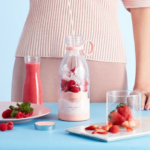 Un FreshJuice Mixeur Portable rempli de lait framboises et entourés de fruits incluant des fraises.