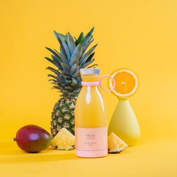 A pink Fresh Juice portable blender filled with yellow juice, surrounded by pineapple, mango and oranges.