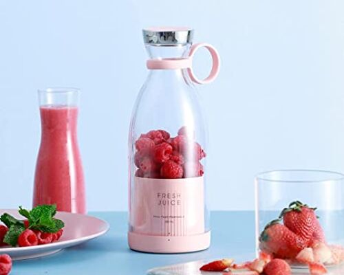 A pink Fresh Juice portable blender filled with raspberries surrounded by a cup filled with strawberries on a blue background.