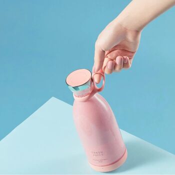 Une main tenant un mixeur portable Fresh Juice rose rempli d'un jus ou smoothie de couleur rose.